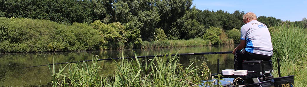 Jan van Schendel op de viskist naast het water met de vaste stok